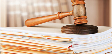 A stack of legal documents with a judge's gavel resting atop