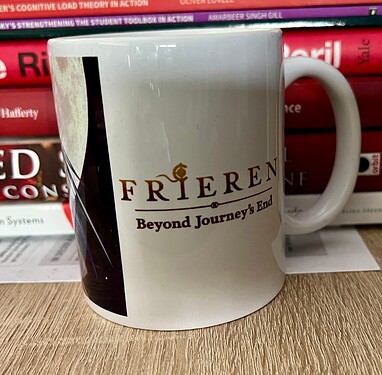 A white mug with the text "FRIEREN Beyond Journey's End" is placed in front of a stack of books. (Captioned by AI)