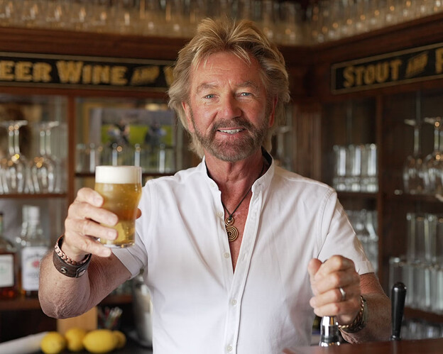 A man in a white shirt raises a glass of beer in a pub setting. (Captioned by AI)