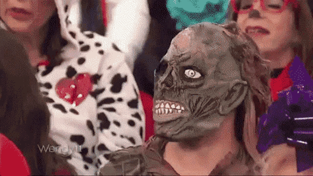 a woman wearing a zombie mask is sitting in a crowd